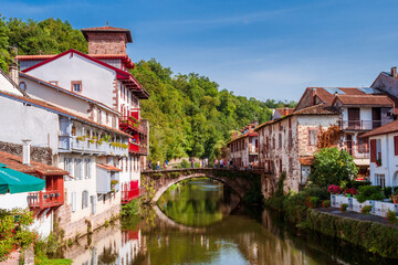 Panoramic view of French white town with red balconies and flowers crossed by a tranquil river. Saint-Jean-Pied-de-Port, France
