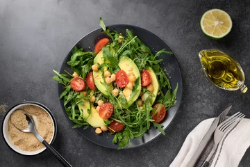 Poster Green salad with avocado, arugula, tomatoes, chickpeas and nutritional yeast flake served on dark plate. Vegan lunch plate. top view © Mila Naumova