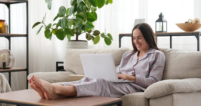 Pleased woman working from home using laptop on sofa 