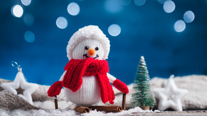 A happy knitted snowman in a winter decoration on skis made of cinnamon sticks. Christmas card.