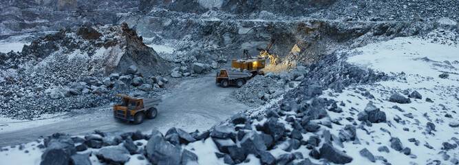 Quarry excavator and quarry dump trucks in the process of loading stone ore in a limestone quarry during night work in the winter, panorama, top view.