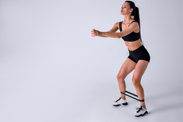 Fototapeta na wymiar caucasian sports fitness woman in sportswear working out with elastic band isolated on white studio background. Sport exercises, healthy lifestyle. Stretching legs, doing lunges. side view portrait