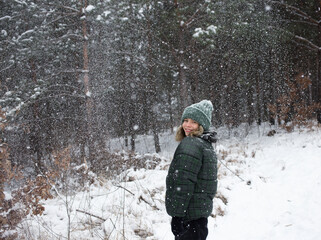 Fototapeta na wymiar teenage girl in a good mood stands in the forest in winter, snowflakes are flying, snowfall