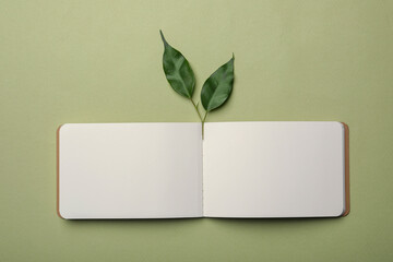 Open notebook and leaves on light green background, flat lay. Personal planning