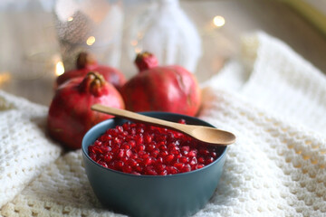 Bowl with fresh pomegranate seeds, pomegranate fruit, knitted blanket and lit candles. Hygge at home. Selective focus.