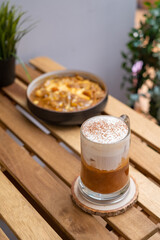 Cappuccino coffee in a transparent cup on a wooden table with nature background