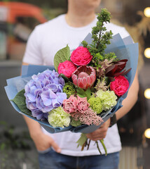 Strong man holding a delicate bouquet of beautiful flowers in his hands. Colorful flower bouquet. Wrapped flowers bouquet.