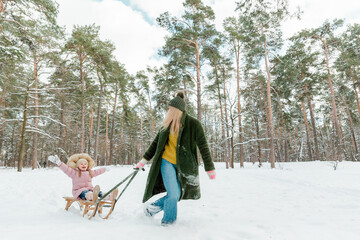 Young beautiful woman with small girl having fun  outside in winter park. Mother and her little daughter sledding outside.