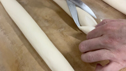 Baker cutting the bread dough with a pair of scissors and with the other one forming the loaf. Concept baker, bread, machine, industry, factory, bakery.