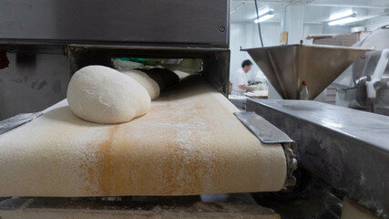 Fototapeta na wymiar Industrial bakery machine making breads. Baker in the background feeding dough to the industrial machine. Concept baker, bread, machine, industry, factory, bakery.