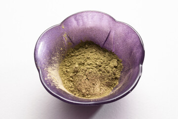 Small purple bowl filled with kratom powder on white background