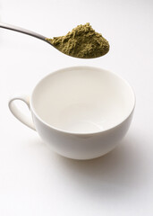 Teaspoon fully filled with kratom powder over empty white cup ready to make kratom drink vertical photo
