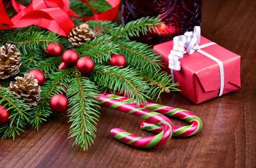 Fototapeta na wymiar Beautiful Christmas still life with candy cane, gift in red box and decorated spruce branches stock images. Christmas spruce twigs with decorations on a wooden background stock photo
