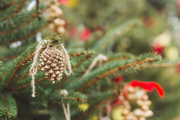 Fototapeta premium Painted gold pine cone on Christmas tree. Diy decoration ideas for children. Environment, reuse, recycle, upcycling and zero waste concept. Selective focus, outdoor no snow background