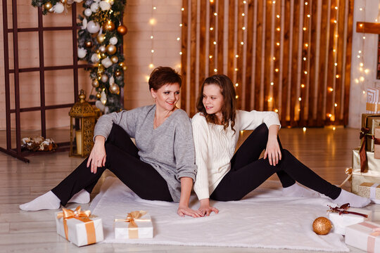 Young Mother And Teenage Daughter Sitting On White Blanket For Christmas