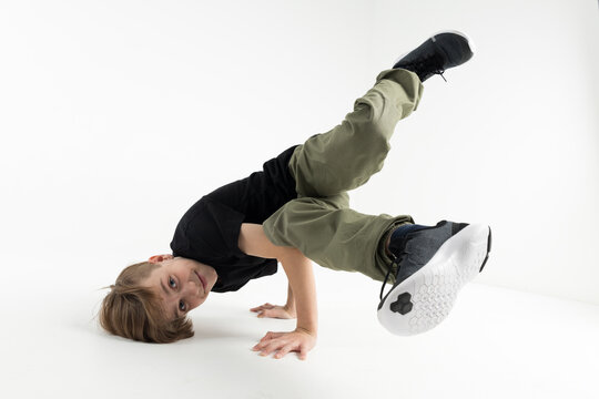 Isolated young cute Russian teenage boy in black t-shirt hip hop break dancer dancing in studio in white background, performing stunt baby freeze of downrock breakdance smiling and looking into camera