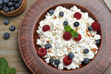 Fresh cottage cheese with berries and mint in plate on wooden table, flat lay