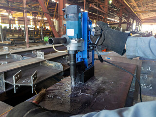 Worker are using a Magnetic Drilling Machine to drill a hole on steel H-beam at industrial factory.