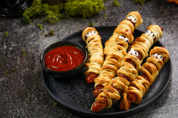 Cute Halloween party snack: wiener sausage with sugar eyes wrapped in dough stripes resembling...