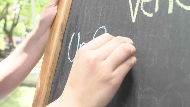Close-Up of a Female Hand Writing "A Venezuelan Spot in Medellin" with Chalk on a Blackboard