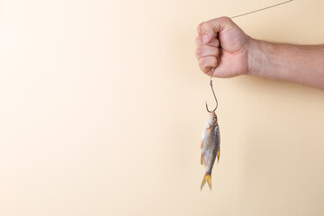 A man's hand holds the fish on a hook, on a yellow background. Concept, template.