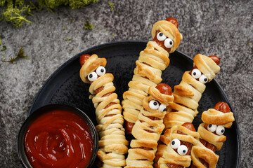 Cute Halloween party snack: wiener sausage with sugar eyes wrapped in dough stripes resembling...