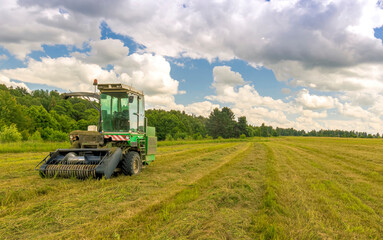 Obraz premium combine harvester gathering harvest on a agricultural field with cloudy sky and green forest on thr background , farm rural landscape