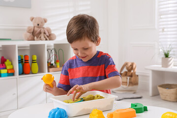Cute little boy playing with bright kinetic sand at table in room