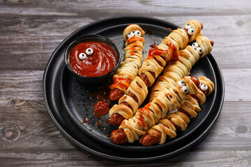 Cute Halloween party snack: wiener sausage with sugar eyes wrapped in dough stripes resembling...
