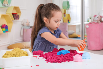 Cute little girl playing with bright kinetic sand at table in room © New Africa
