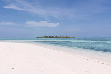 Fototapeta na wymiar Playa paradisiaca soleada, agua cristalina y cielo azul, isla al fondo