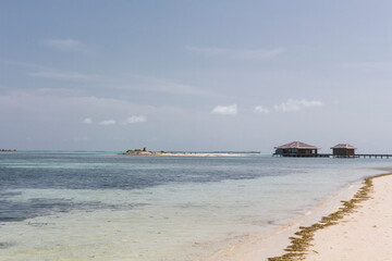 Playa paradisiaca soleada, agua cristalina y cielo azul, cabañas de fondo