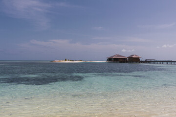 Playa paradisiaca soleada, agua cristalina y cielo azul, con cabañas al fondo