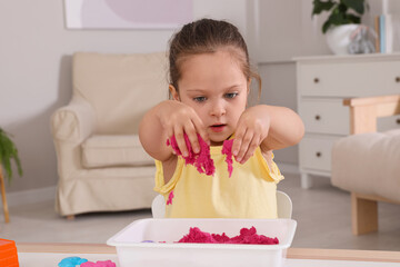 Cute little girl playing with bright kinetic sand at table in room