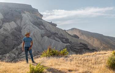 Fototapeta premium Portrait of adult man in cowboy hat in desert area against mountain and blue sky