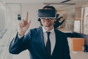 Young successful businessman in VR goggles touching air with finger during virtual business meeting
