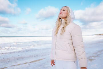 Woman wearing white clothes feels the cold on winter sea coast. Female breathe with cold fresh air...