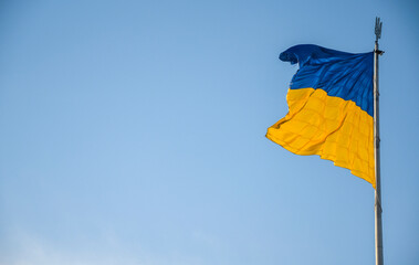 National flag of Ukraine on flagpole waving in the wind with blue clearly sky on background. Freedom and patriotism concept