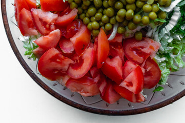 Salad with tomatoes and green peas in a glass bowl on a white background. Top view.