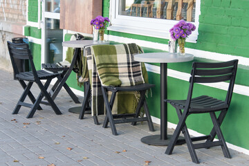 Empty chairs in outdoor cafe or restaurant. Wooden tables and chairs at sidewalk cafe. Autumn in city, plaids on chairs and tables of a street cafe
