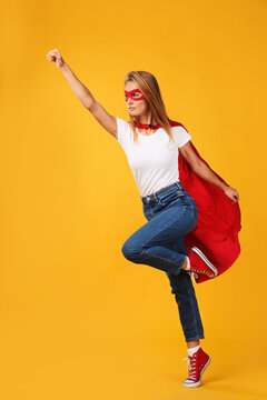 Confident woman wearing superhero cape and mask on yellow background