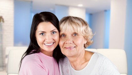 Happy smiling mature mother embracing grownup daughter, having fun, sitting on cozy couch