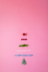 Christmas tree made of office equipment, christmas decoration, plant leaf, and shine object. Pink background. Holidays idea. New year concept. 
