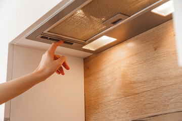 Woman hand turn on embedded cooker hood in white modern kitchen