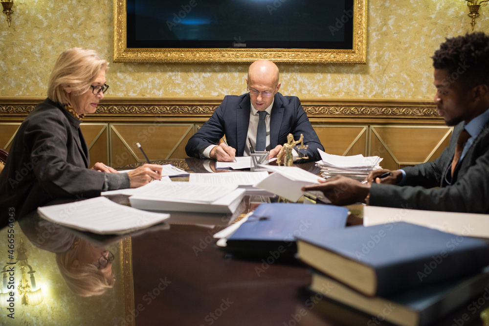 Aufkleber mature and young intercultural lawyers working with papers and signing them while sitting by large t