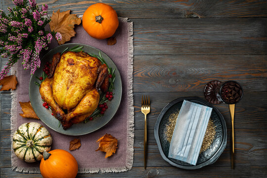 Roasted chicken or turkey for Thanksgiving Day on festive table setting with protective mask on wooden table. Fried chicken, pumpkins for Thanksgiving dinner. Thanksgiving Day in pandemic covid 19