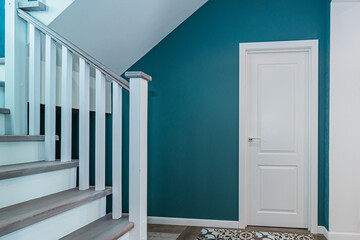 Fragment of a room with a white door, turquoise walls and a wooden staircase