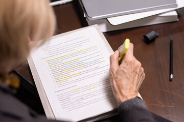 Hand of mature female lawyer highlighting lines depicting the main points of contract or other...