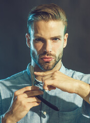 Hairdresser demonstrating sharp blade of barbershop accessory. Professional barber with beard and mustache holds straight razor. Handsome bearded hairdresser in stylish clothes holding dangerous razor