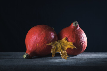 Two pumpkins and a maple leaf on a dark background